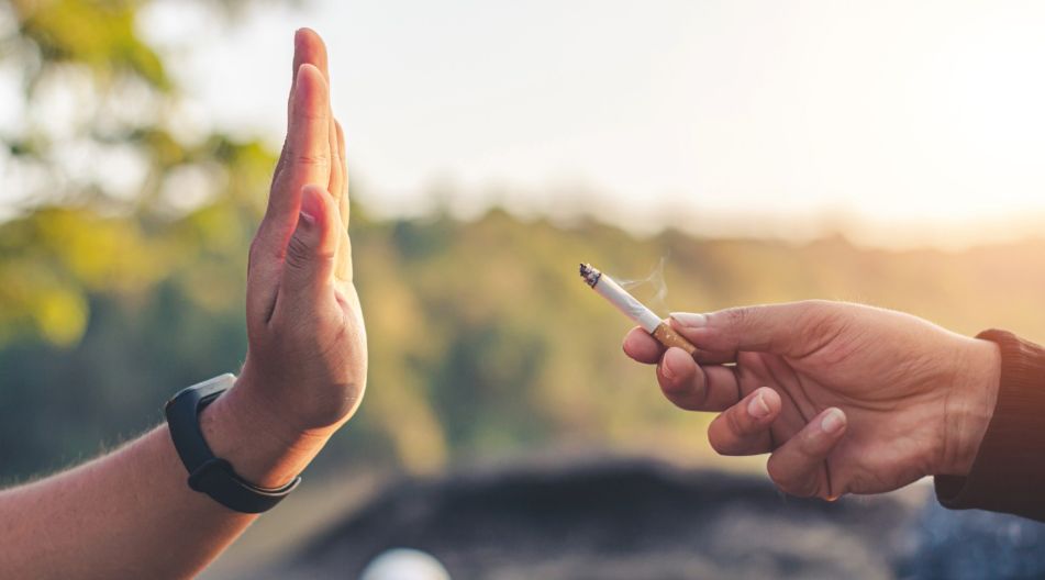 Eine Person bietet eine brennende Zigarette an, während eine andere mit erhobener Hand ablehnend das Rauchen verweigert.
