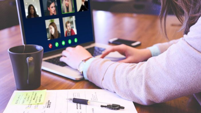 Das Bild zeigt eine Person, die an einem Laptop sitzt und an einer Videokonferenz teilnimmt. Auf dem Bildschirm sind mehrere Personen in einem virtuellen Meeting sichtbar. Im Vordergrund befinden sich Notizen, ein Stift und eine Tasse Kaffee. Das Bild zeigt eine Person, die an einem Laptop sitzt und an einer Videokonferenz teilnimmt. Auf dem Bildschirm sind mehrere Personen in einem virtuellen Meeting sichtbar. Im Vordergrund befinden sich Notizen, ein Stift und eine Tasse Kaffee.