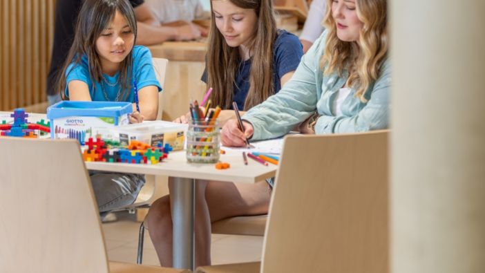 Kinder sitzen in einer Kita an einem Tisch und malen zusammen in einem kreativ gestalteten Raum.
