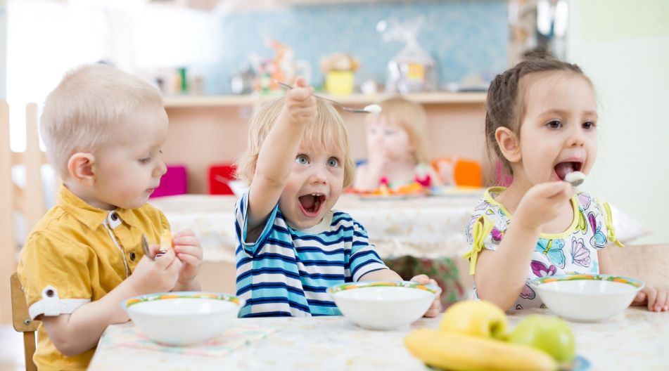 Drei Kinder sitzen am Tisch und essen mit Begeisterung aus Schüsseln.